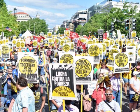 Photo of crowd filling the street on June 18, many holding Poor People's Campaign signs in yellow, black and white with slogans like Forward Together, Lucha Contra La Pobreza, Everybody Has the Right to Live.