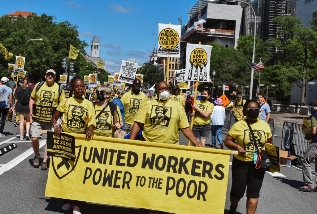 Photo of United Workers members at June 18 wearing in yellow and black t-shirts with Harriet Tubman's image. They are holding a yellow banner with black lettering that reads "United Workers, Power to the Poor."
